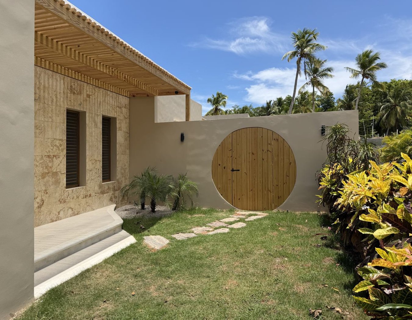 L'entrée : façade en pierre de corail, pergola et porte ronde sur le jardin clos — Villas Origen