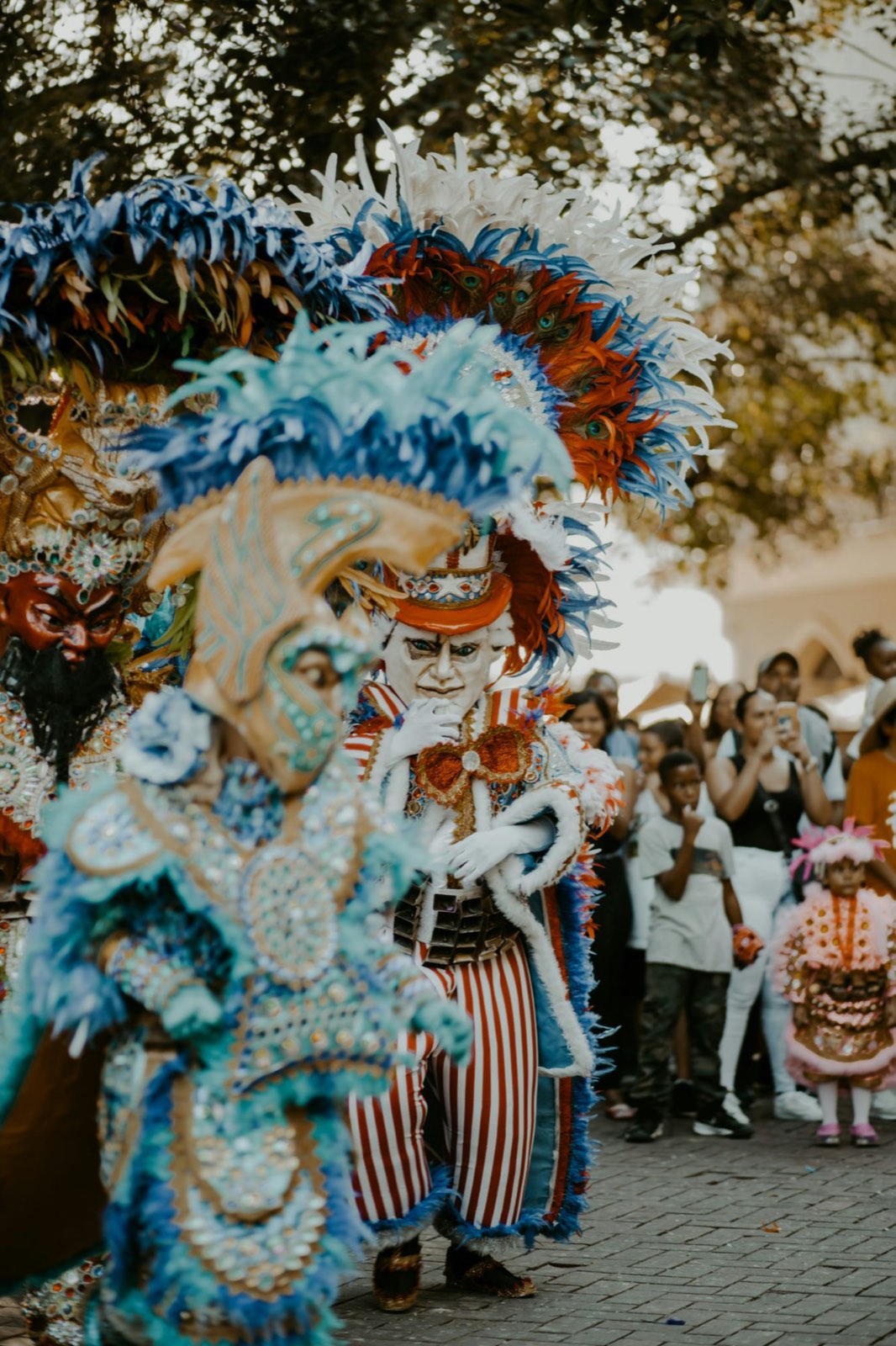 Personnages masqués du Carnaval dominicain en costumes de plumes colorées, devant une foule de spectateurs