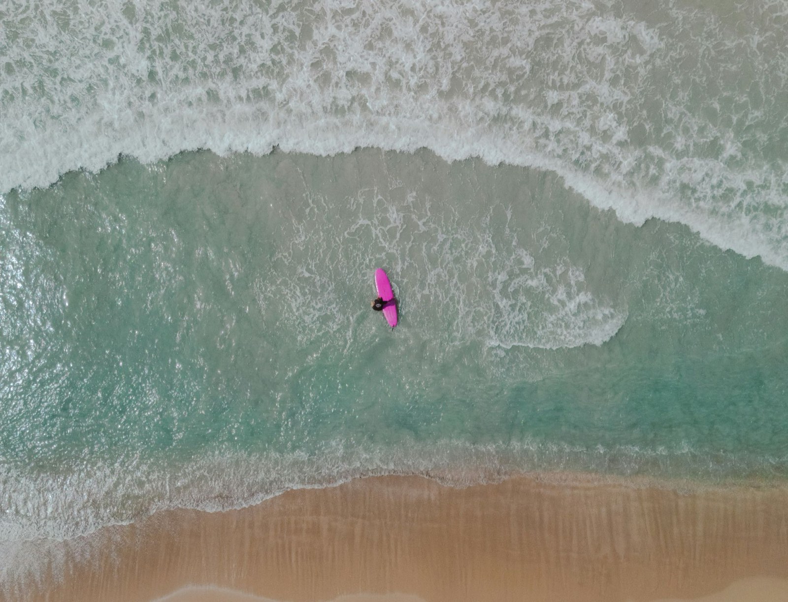 Vue du ciel d'une surfeuse sur sa planche rose dans les vagues turquoise d'une plage de Las Terrenas